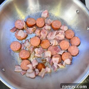 Southern Fried Cabbage Recipe with Bacon and Onions 4 Sausage and bacon cooking in a pan.