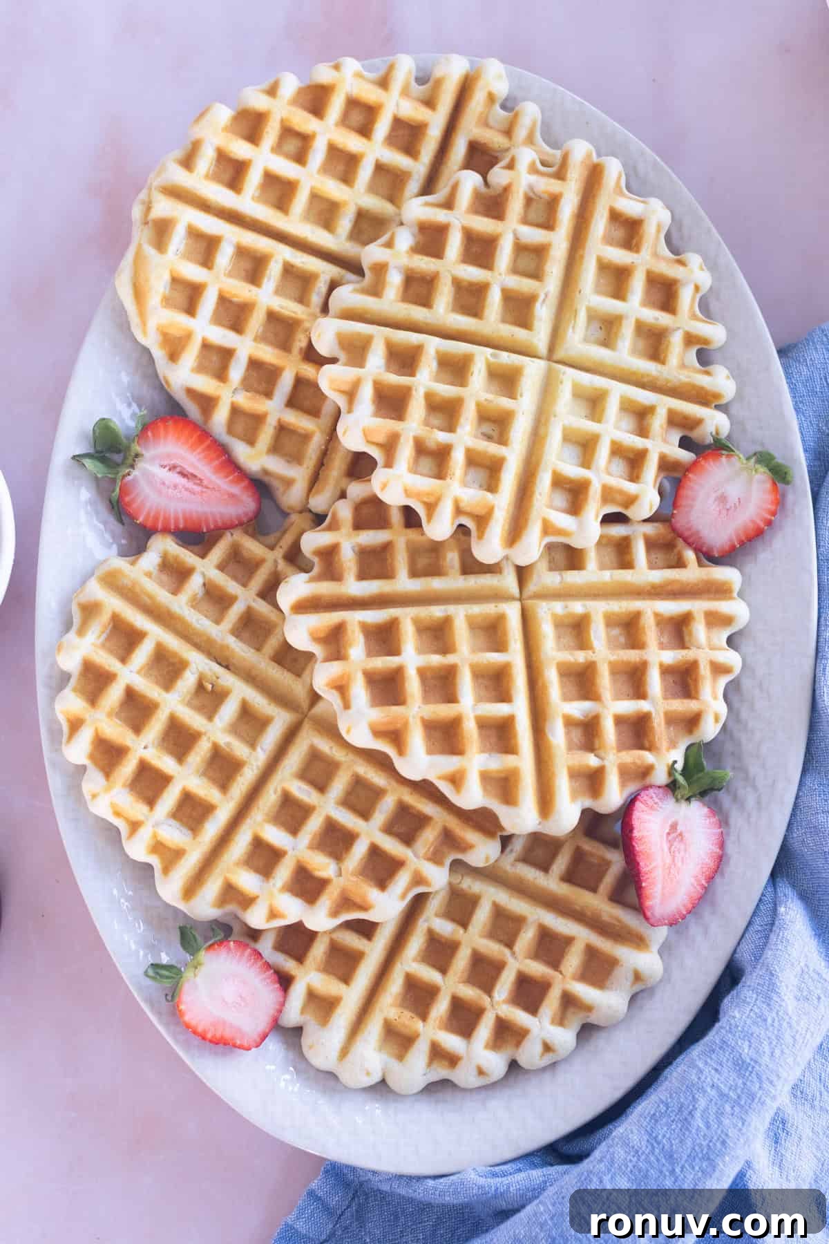 Fluffy Homemade Waffles Recipe 2 A white platter with five homemade waffles garnished with fresh strawberry slices.