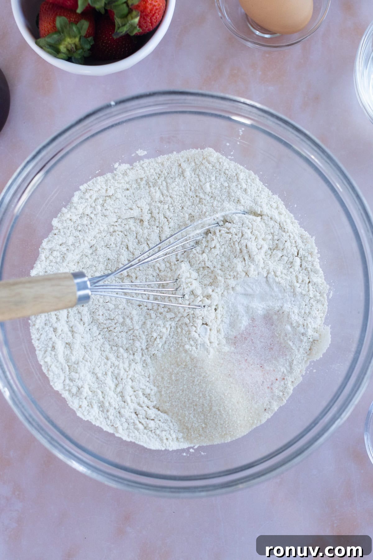 Fluffy Homemade Waffles Recipe 5 Overhead view of a glass bowl filled with flour and sugar being mixed with a whisk.