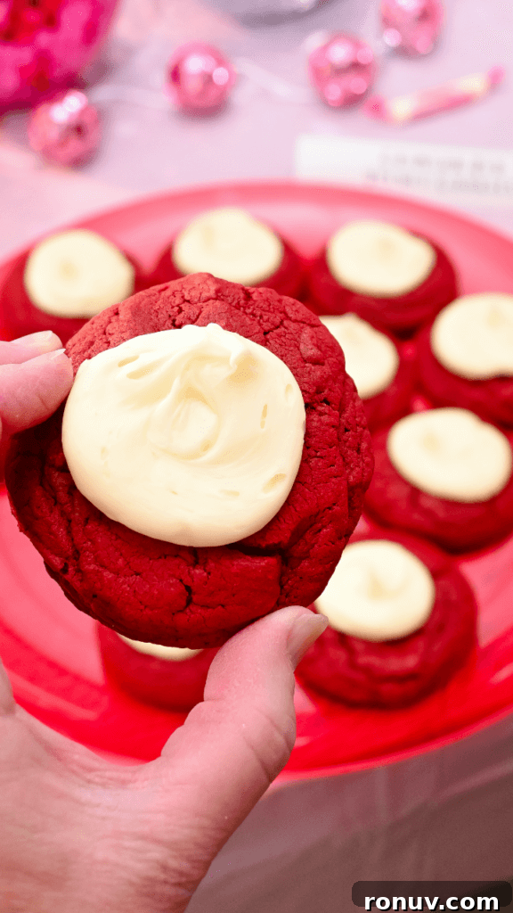 Red Velvet Cake Mix Cookies with Cream Cheese 3 A hand holding a red velvet cake mix cookie over a red platter full of cookies.