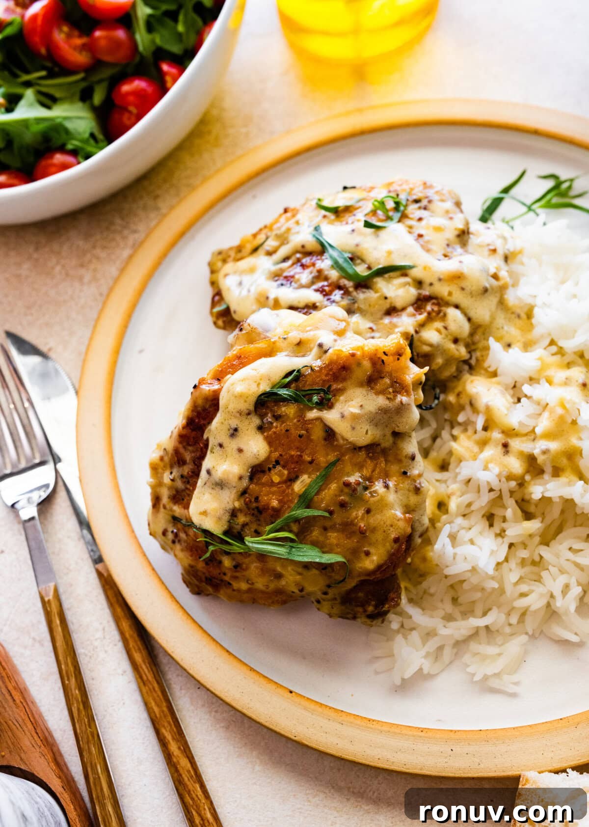 Pan-Seared Chicken Thighs in Creamy Mustard Sauce 3 plated chicken with mustard sauce and a side of rice. Fork and knife next to the plate.