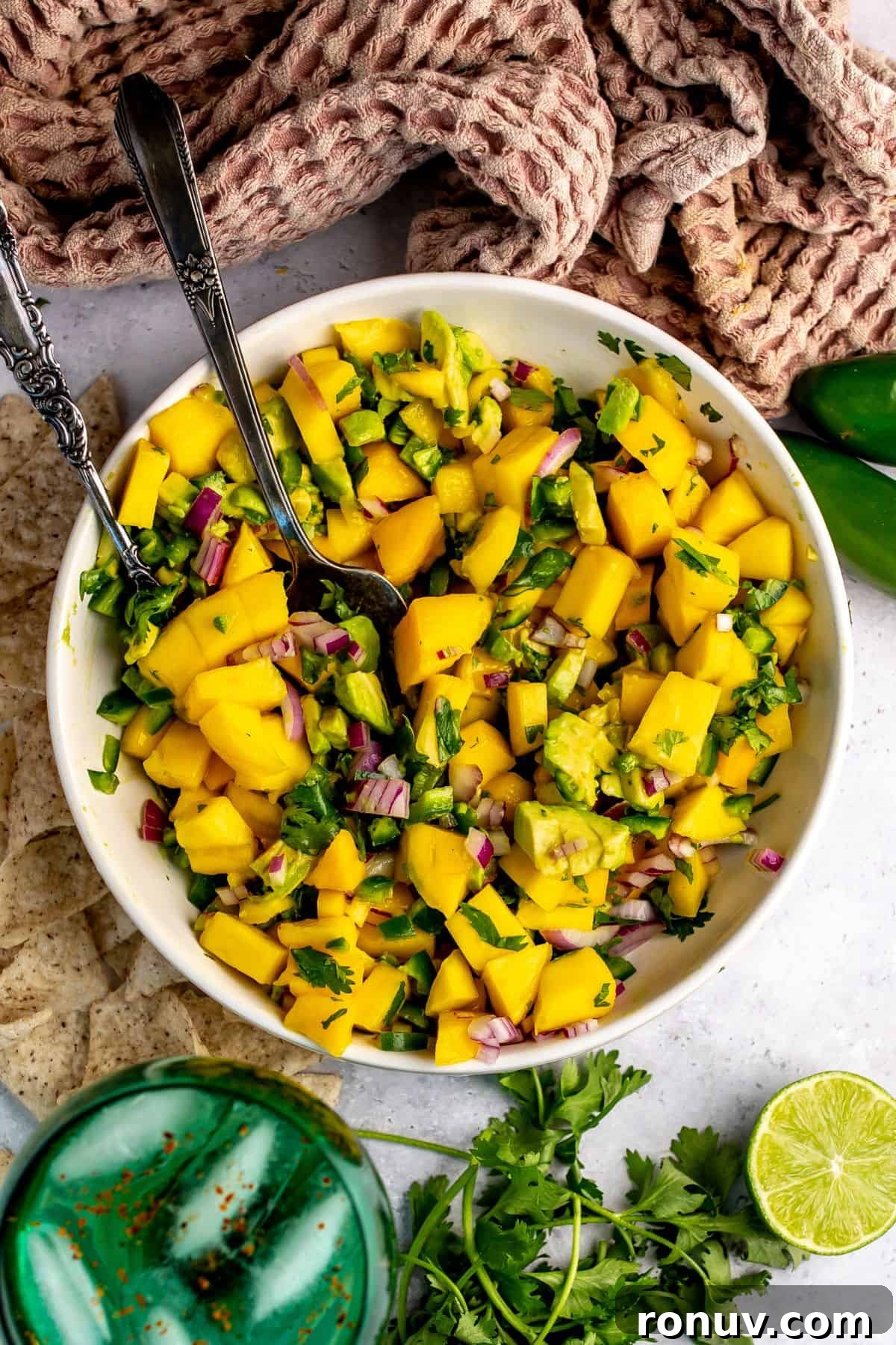 Zesty Mango and Avocado Salsa with Lime 2 Mango and Avocado Salsa in a white bowl with a spoon in it and a green glass.