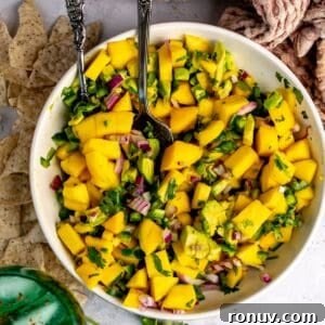 Mango and Avocado Salsa in a white bowl with a spoon in it and a green glass.