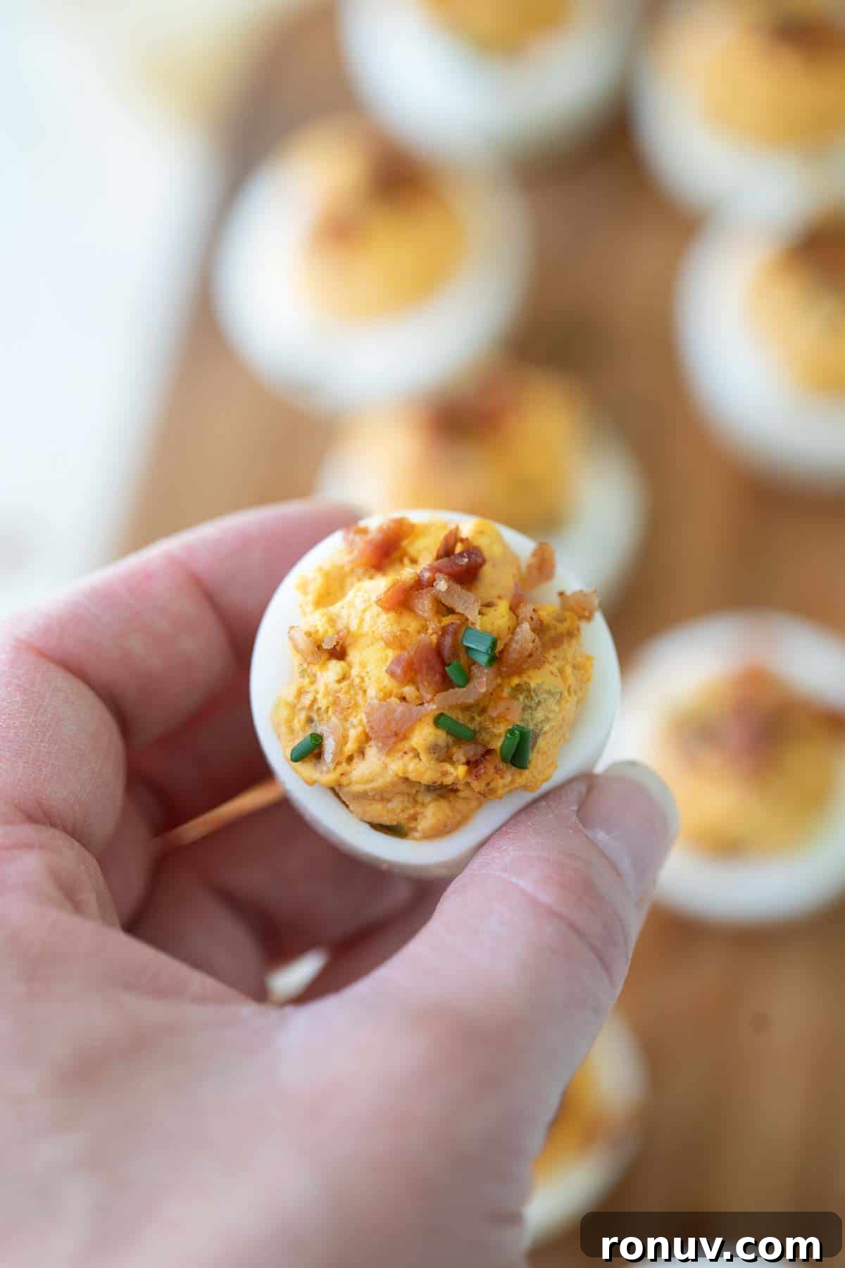 Deviled Egg with Bacon Hand holding a deviled egg with bacon.