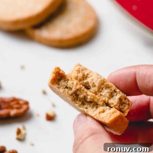 Classic Pecan Sandies Recipe 8 Pecan sandies cookies broken in half and hand held.
