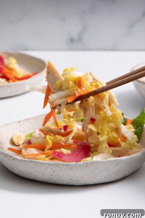 Vietnamese Chicken Salad with Tangy Nuoc Cham Dressing 5 Vietnamese chicken salad in a speckled white bowl, being picked up with chopsticks against a soft, light-toned white and gray background.