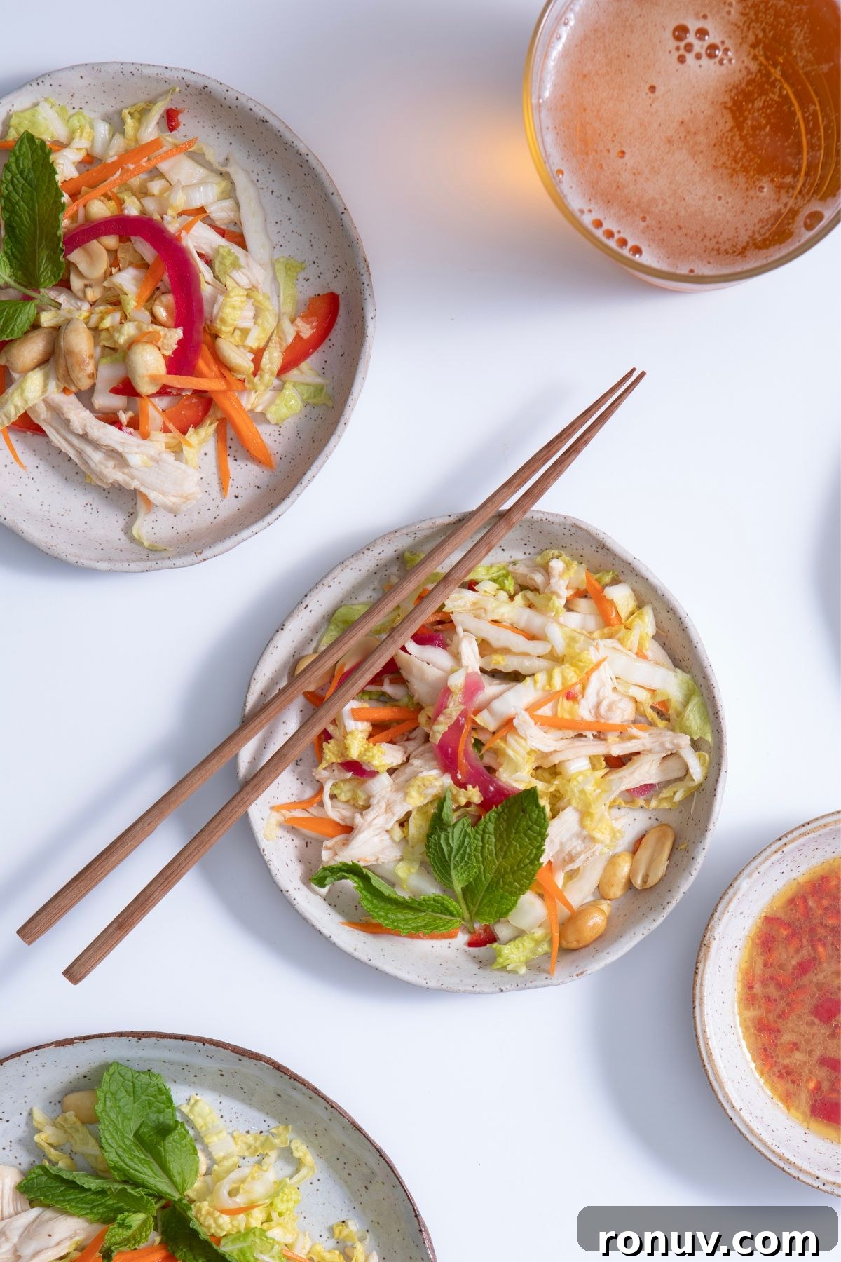 Vietnamese Chicken Salad with Tangy Nuoc Cham Dressing 7 Three shallow speckled white bowls filled with Vietnamese chicken salad, garnished with fresh herbs. Chopsticks rest on the main bowl, all set against a clean white background