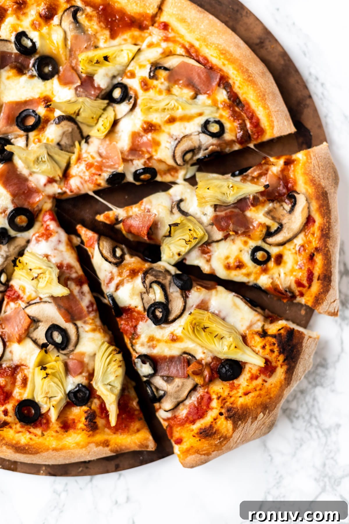 Authentic Capricciosa Pizza Recipe 2 A top down view of sliced pizza capricciosa on a pizza stone.