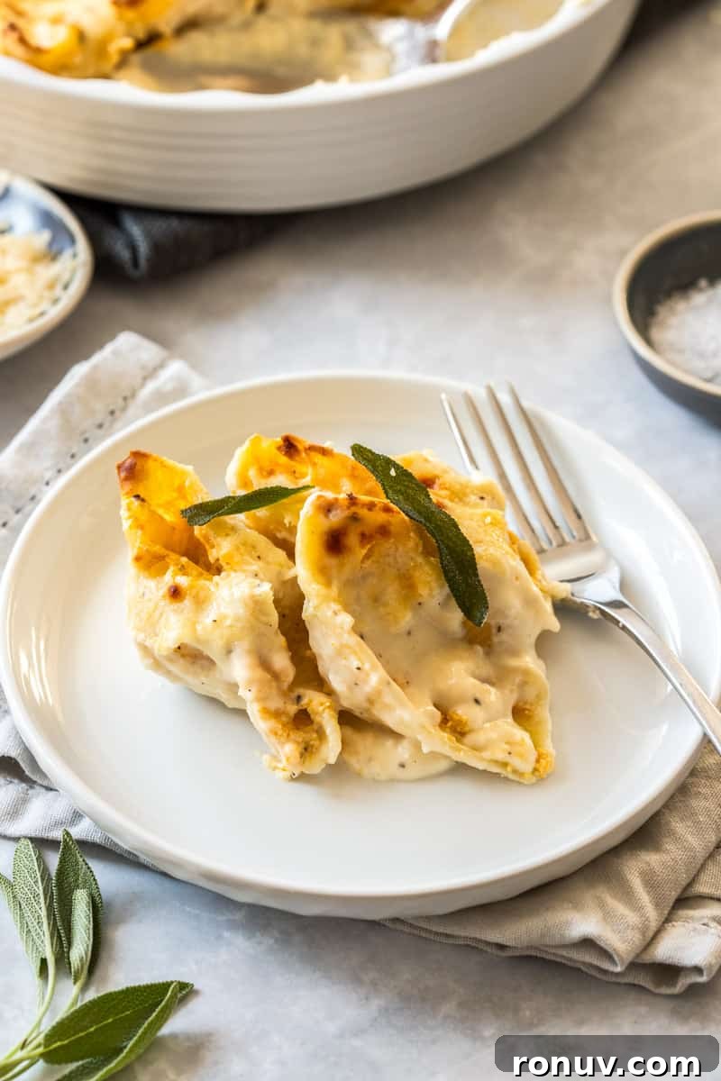 Creamy Pumpkin Ricotta Stuffed Shells Recipe 7 Serving of three pasta shells on a round white plate, with a fork on the edge, and some sage leaves in the corner.