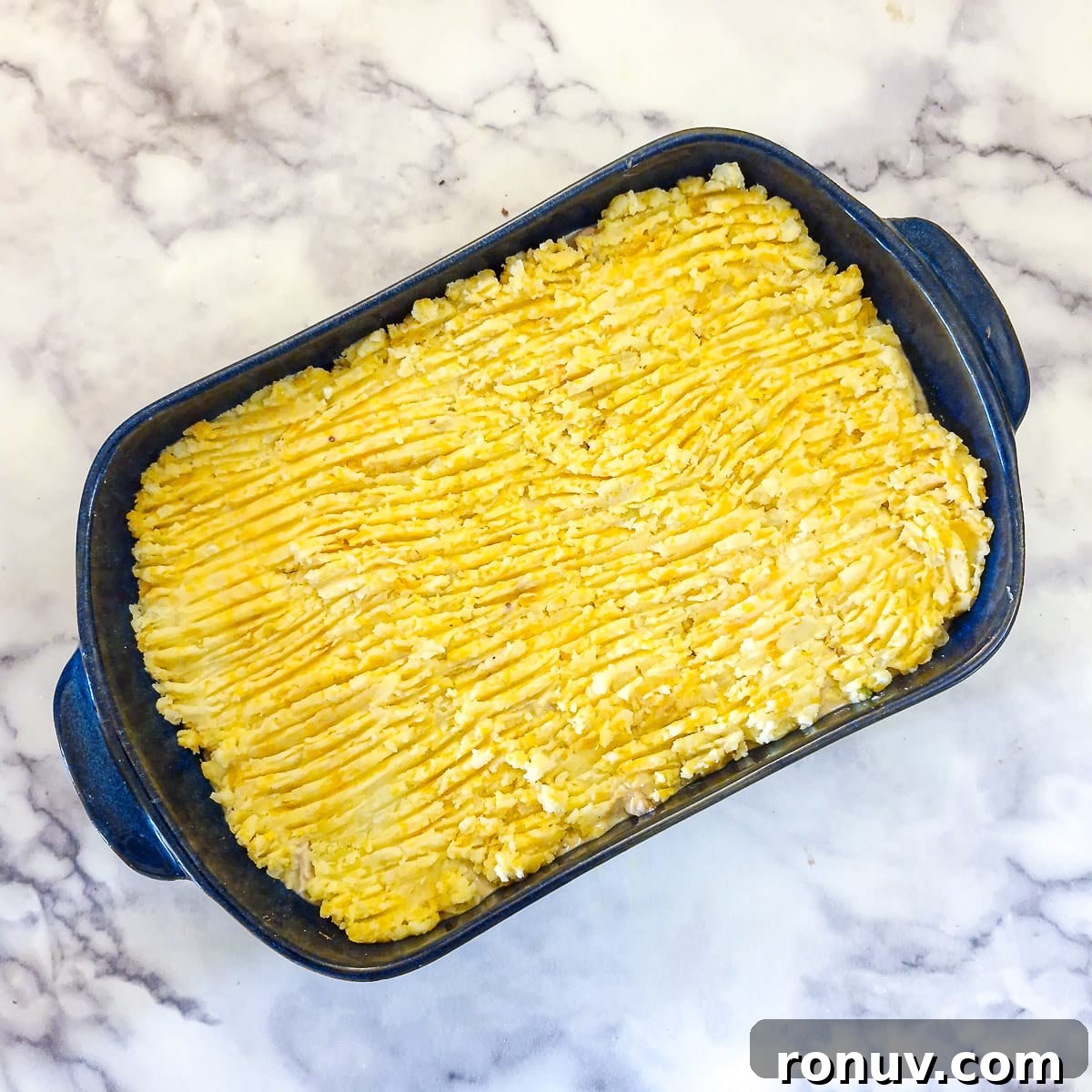Turn Leftover Chicken Into Shepherd's Pie 13 Potato mash that has been smoothed out with a fork on top of the chicken filling in a blue baking dsh.