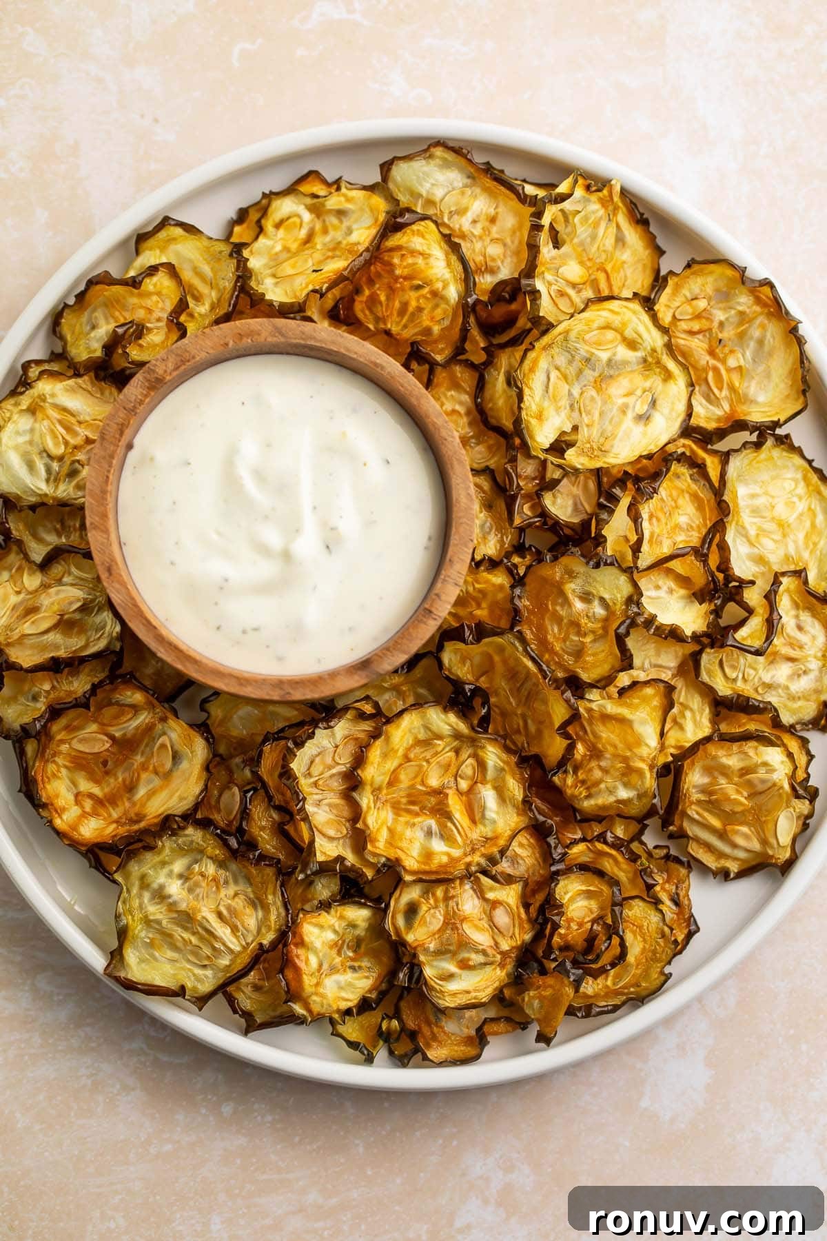 Crispy Oven-Baked Cucumber Chips Recipe 3 Crispy cucumber chips arranged around a bowl of ranch dressing on a large rimmed plate.