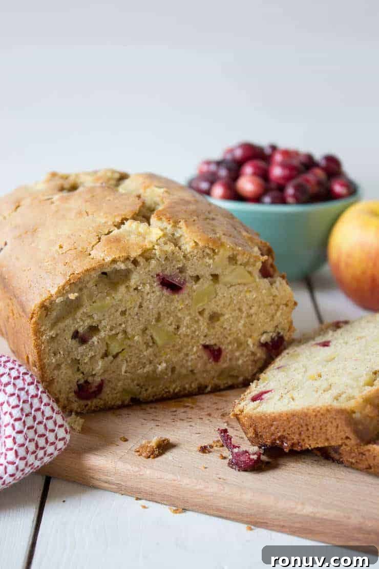 Moist Cranberry Apple Bread Recipe 2 A loaf of bread filled with cranberries and apples on a wooden cutting board.