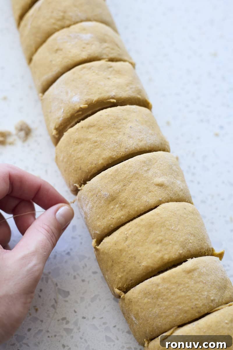 Pumpkin Cinnamon Rolls Recipe with Sourdough Discard 9 A hand pinch cutting the rolls with dental floss.