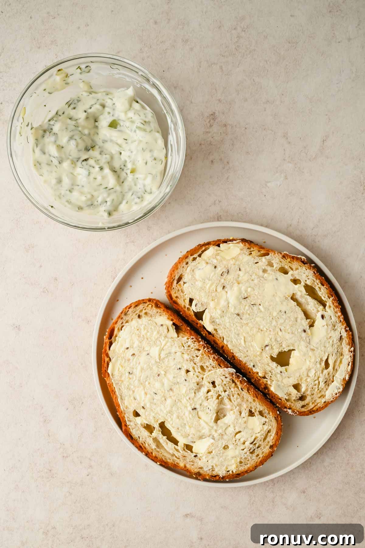 Salmon BLT Sandwich Recipe with Avocado & Lemon-Dill Mayo 5 two slices of bread spread with butter beside a bowl of aioli.