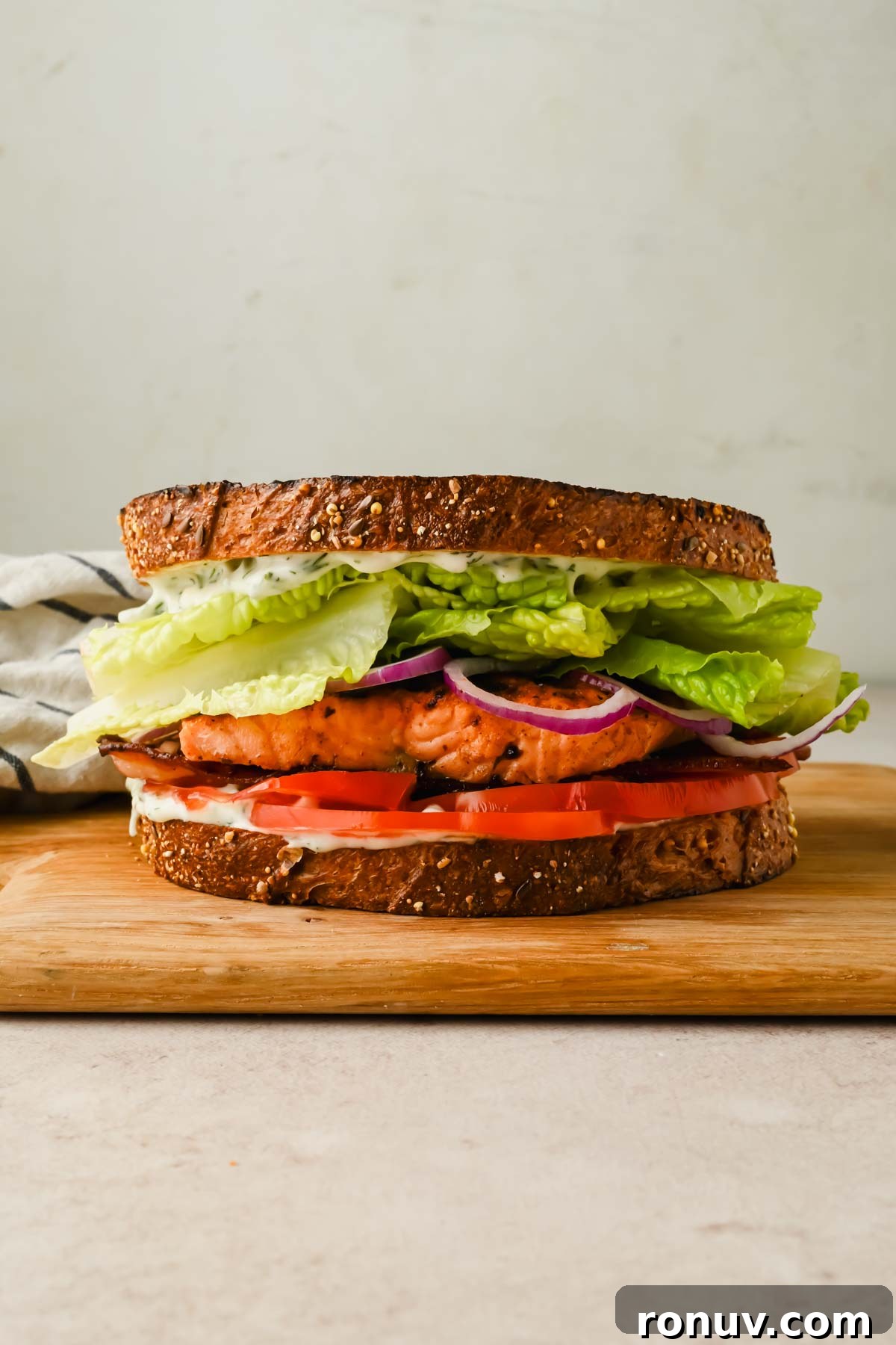 Salmon BLT Sandwich Recipe with Avocado & Lemon-Dill Mayo 8 Salmon sandwich stacked with lettuce, bacon and tomato on toasted sourdough bread.