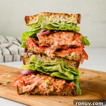Salmon BLT Sandwich Recipe with Avocado & Lemon-Dill Mayo 9 two stacked halves of a salmon BLT on a wood cutting board.