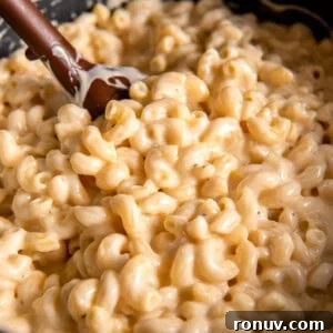 A large pot filled with creamy gouda mac and cheese. A wooden spoon scoops some of the mac and cheese out of the pot.