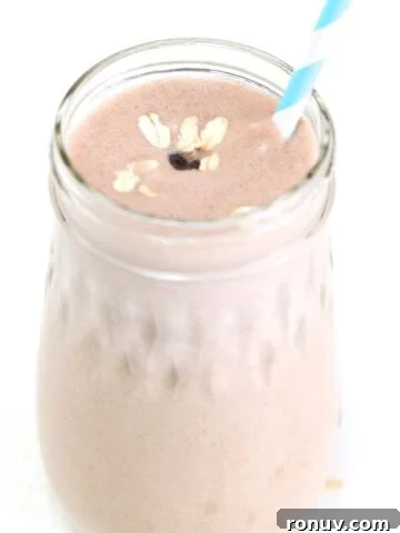 One Peanut Butter Banana Oatmeal Smoothie in a glass jar topped with oats and a mini chocolate chip, served with a straw.