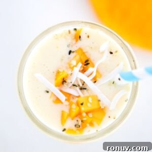 Tropical Mango Pineapple Smoothie Recipe 10 Creamy Mango Pineapple Smoothie topped with mango and coconut flakes with a blue and white striped straw.