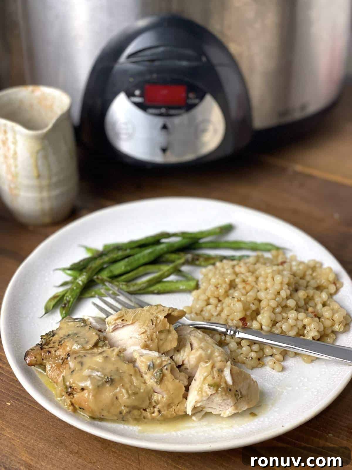 Slow-Cooker Turkey Tenderloins in Honey Mustard Gravy 2 A cut up honey mustard turkey tenderloin with Israeli couscous and green beans on a plate with a fork in front of a crockpot.