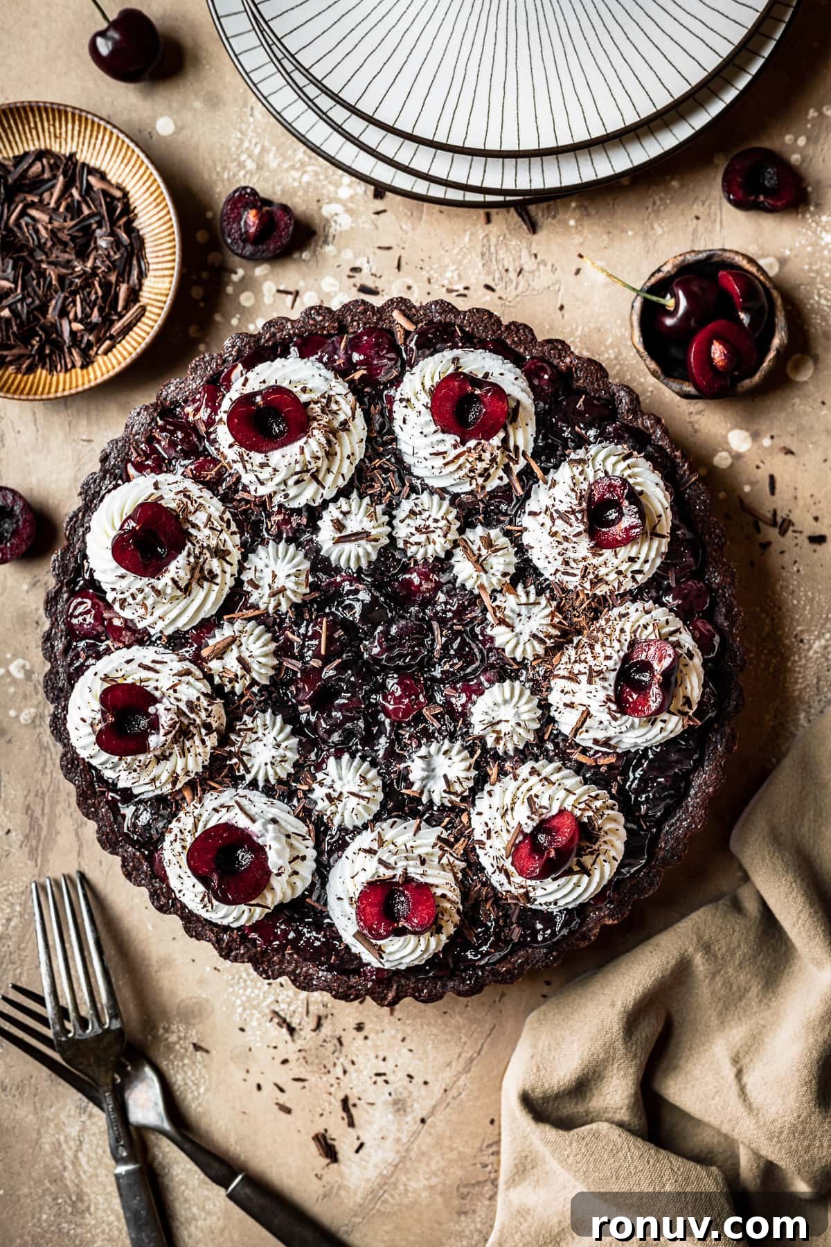 Decadent Chocolate Cherry Tart Recipe 2 A chocolate cherry tart with piped whipped cream swirls, cherry halves, and chocolate shavings.