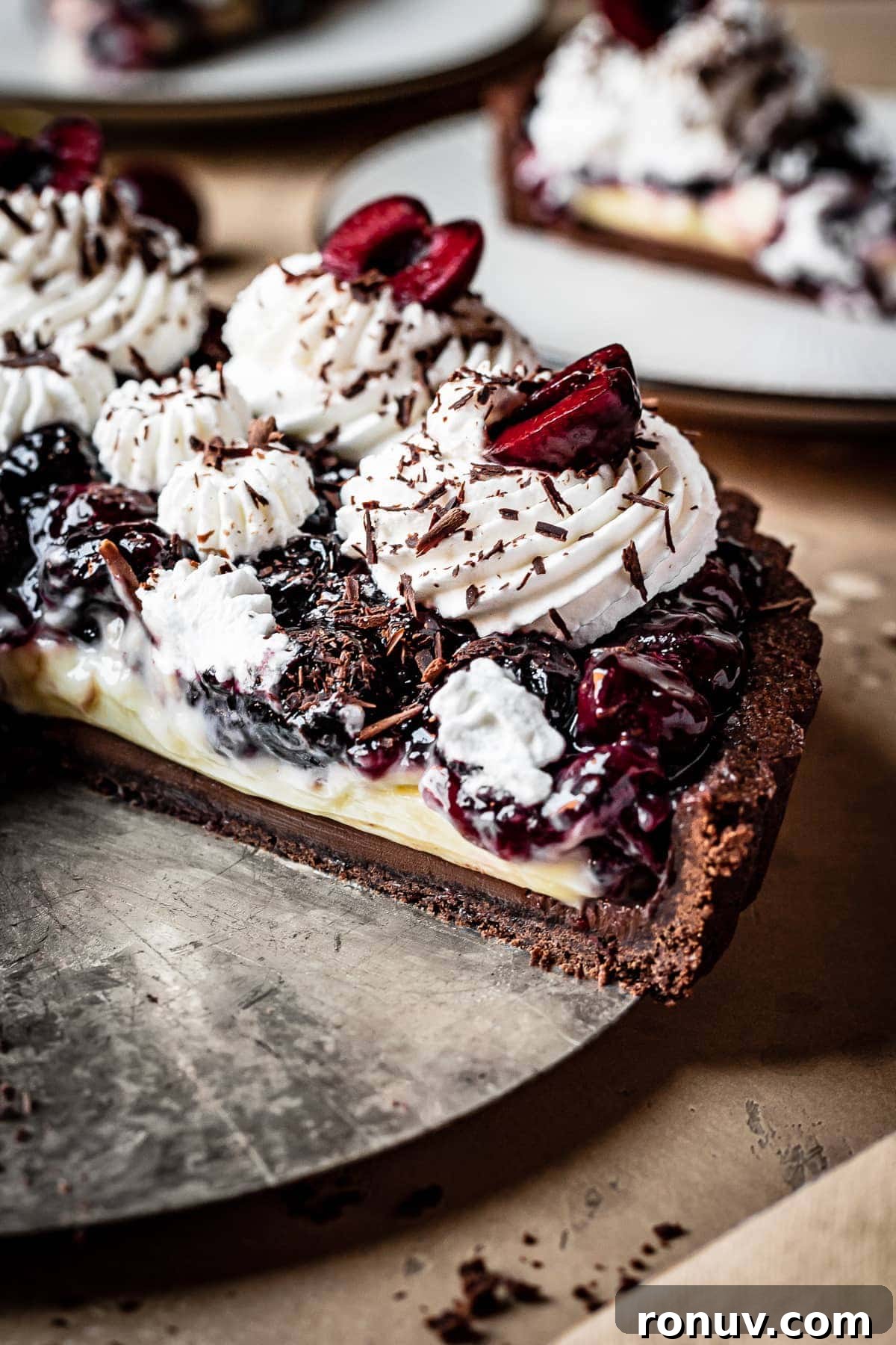 Decadent Chocolate Cherry Tart Recipe 6 The sliced interior of a cherry chocolate pastry cream tart, with whipped cream piping and cherries on top.