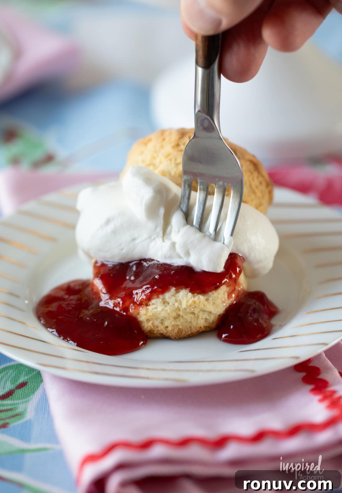 Classic Buttery Homemade Scones Recipe 14 hand with fork taking a bite of scone filled with jam and whipped cream.