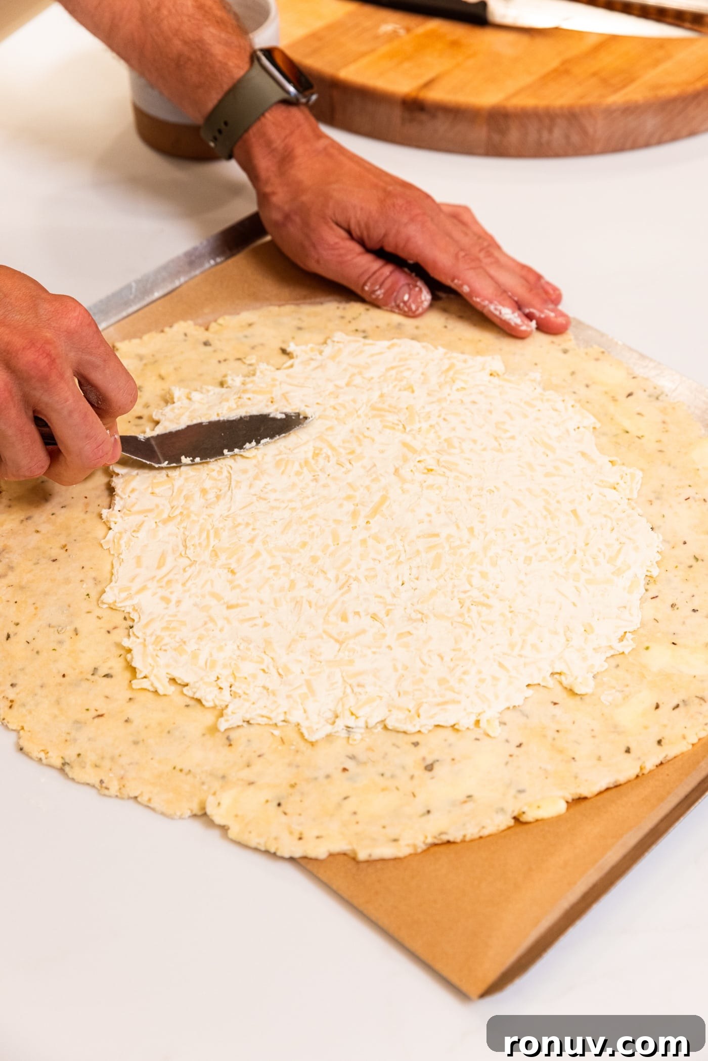 Fresh Tomato Galette Recipe with Basil 12 Hand using offset spatula to spread cream cheese mixture on top of unbaked dough on baking sheet.