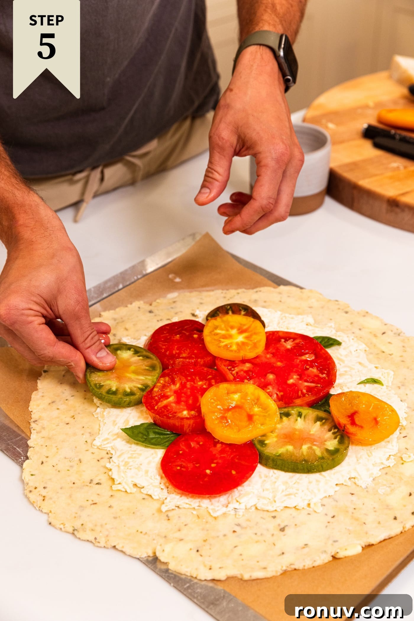 Fresh Tomato Galette Recipe with Basil 13 Hand placing slices of tomatoes on top of cream cheese mixture on unbaked dough.