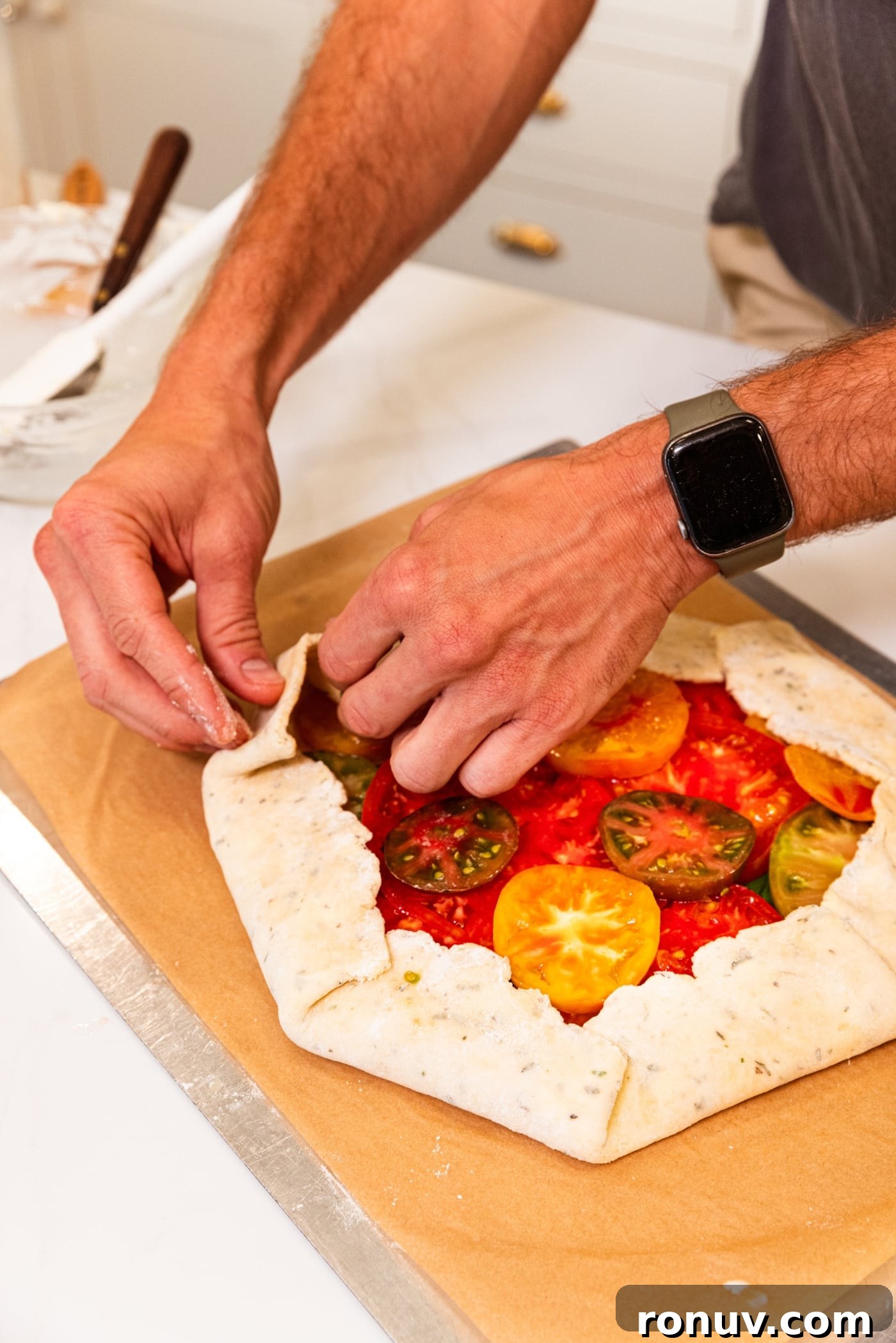 Fresh Tomato Galette Recipe with Basil 14 Hand pressing dough for a tomato galette with fresh slices of tomato all on baking sheet.