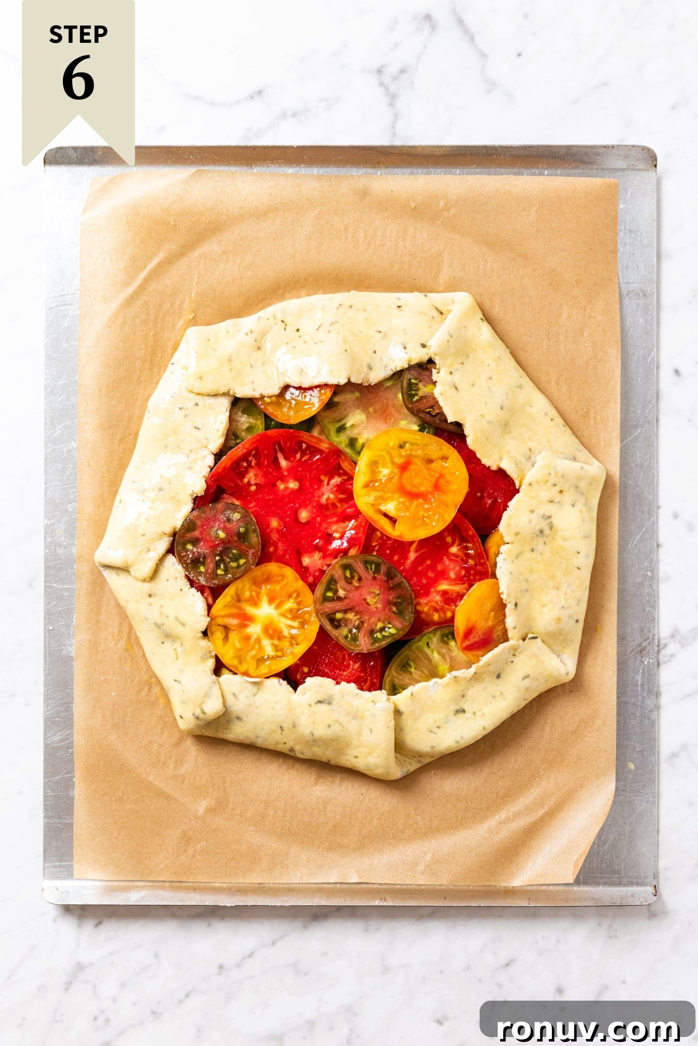 Fresh Tomato Galette Recipe with Basil 15 Unbaked tomato galette sitting on piece of brown parchment on a baking sheet before going into the oven to bake.