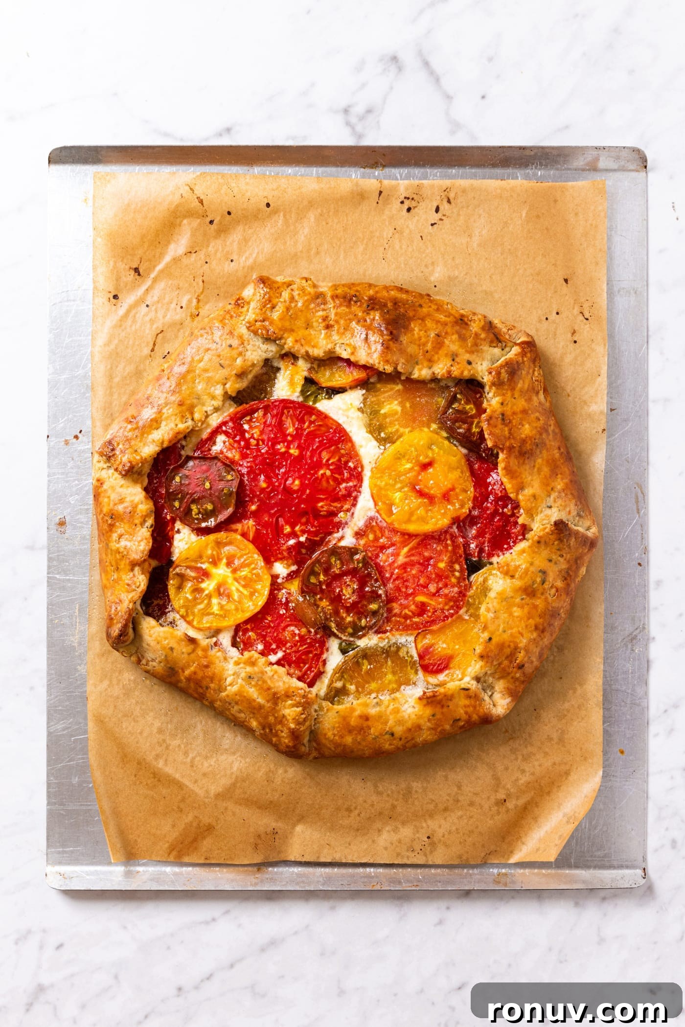 Fresh Tomato Galette Recipe with Basil 16 Baked tomato galette with golden brown edges sitting on piece of parchment paper on baking sheet right after coming out of the oven.