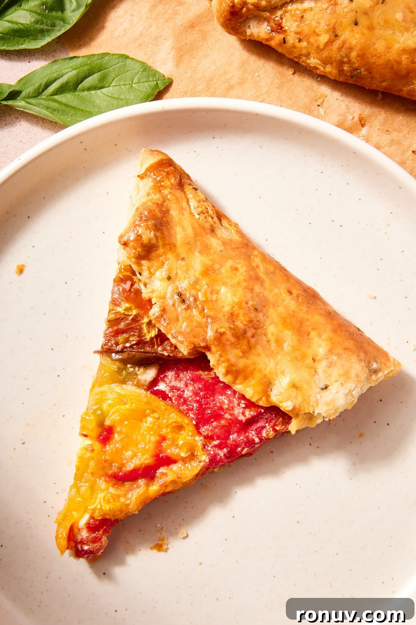 Fresh Tomato Galette Recipe with Basil 3 Slice of fresh tomato galette sitting on white plate with flaky browned crust.