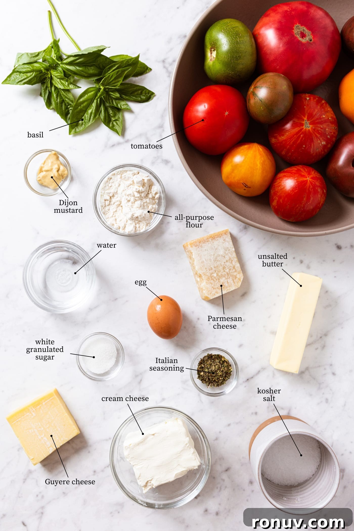 Fresh Tomato Galette Recipe with Basil 4 White marble surface filled with all ingredients needed to make a fresh tomato galette including tomatoes, basil, flour, egg, cheese, and more.