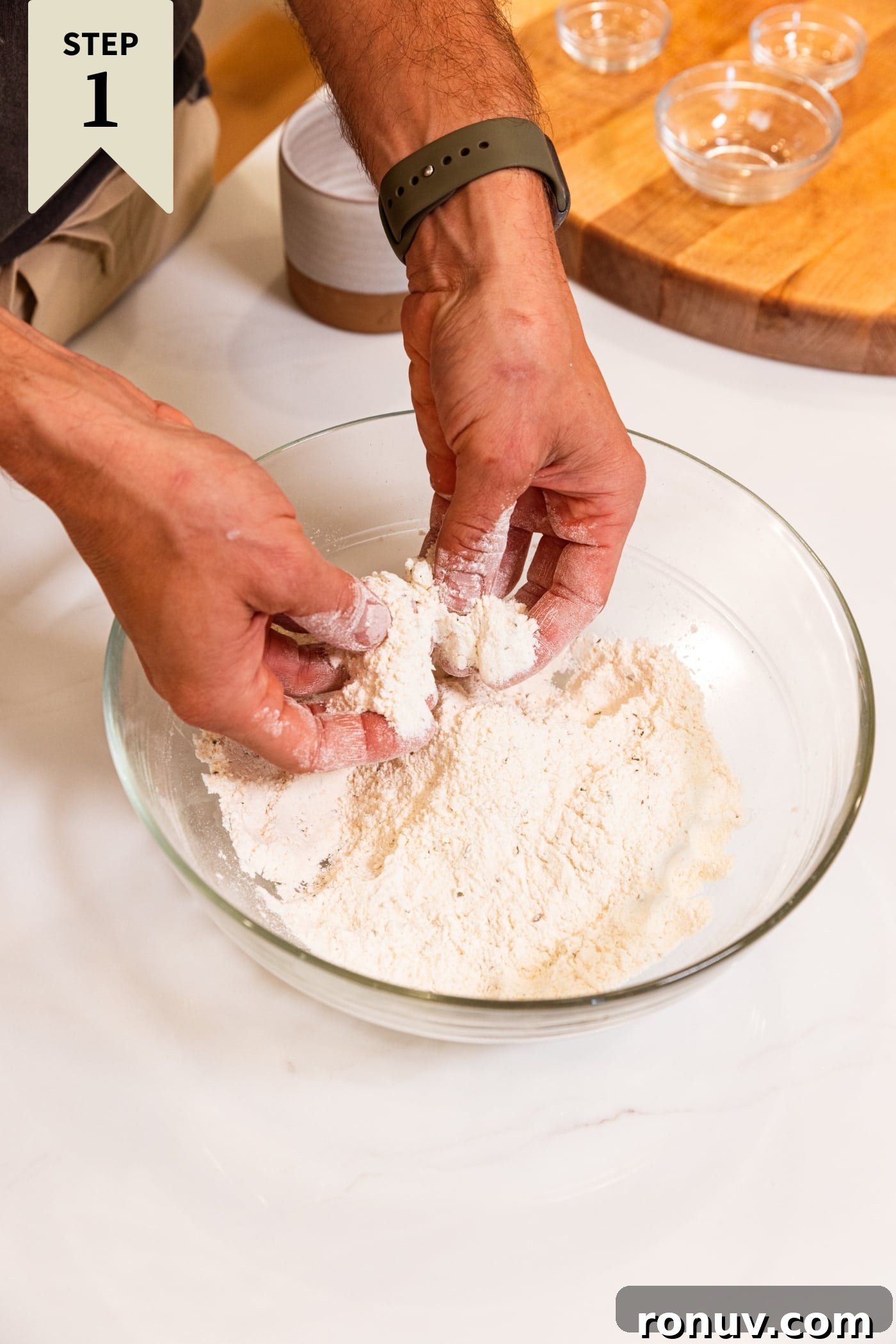 Fresh Tomato Galette Recipe with Basil 5 Two hands mixing together flour in a glass bowl on white surface with wood cutting board in background.