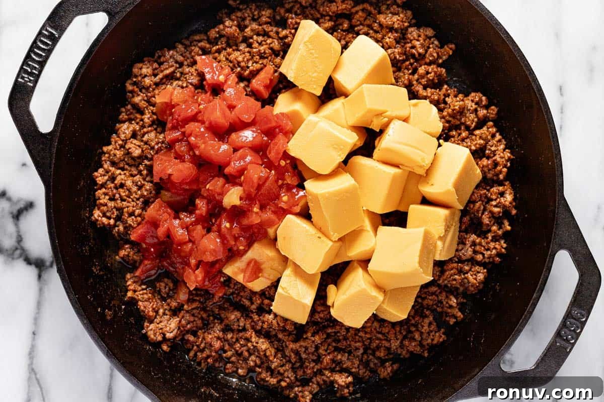Creamy Cheesy Rotel Dip Recipe 5 Cast iron skillet with taco meat, Rotel tomatoes, and diced Velveeta cheese.