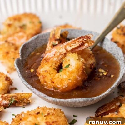 Two baked coconut shrimp sitting in a dish of apricot dipping sauce.