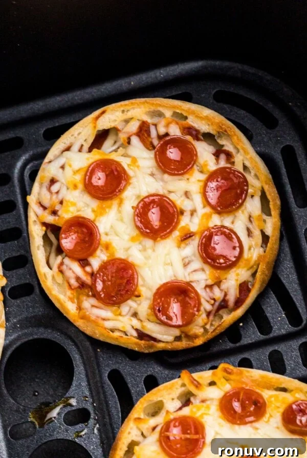 Golden crispy english muffin pizzas with melted cheese and cooked pepperonis in an air fryer basket.