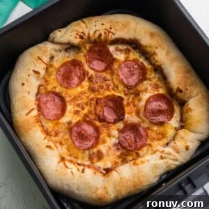 Air fryer pizza that has been fully cooked and is in the basket of the air fryer.