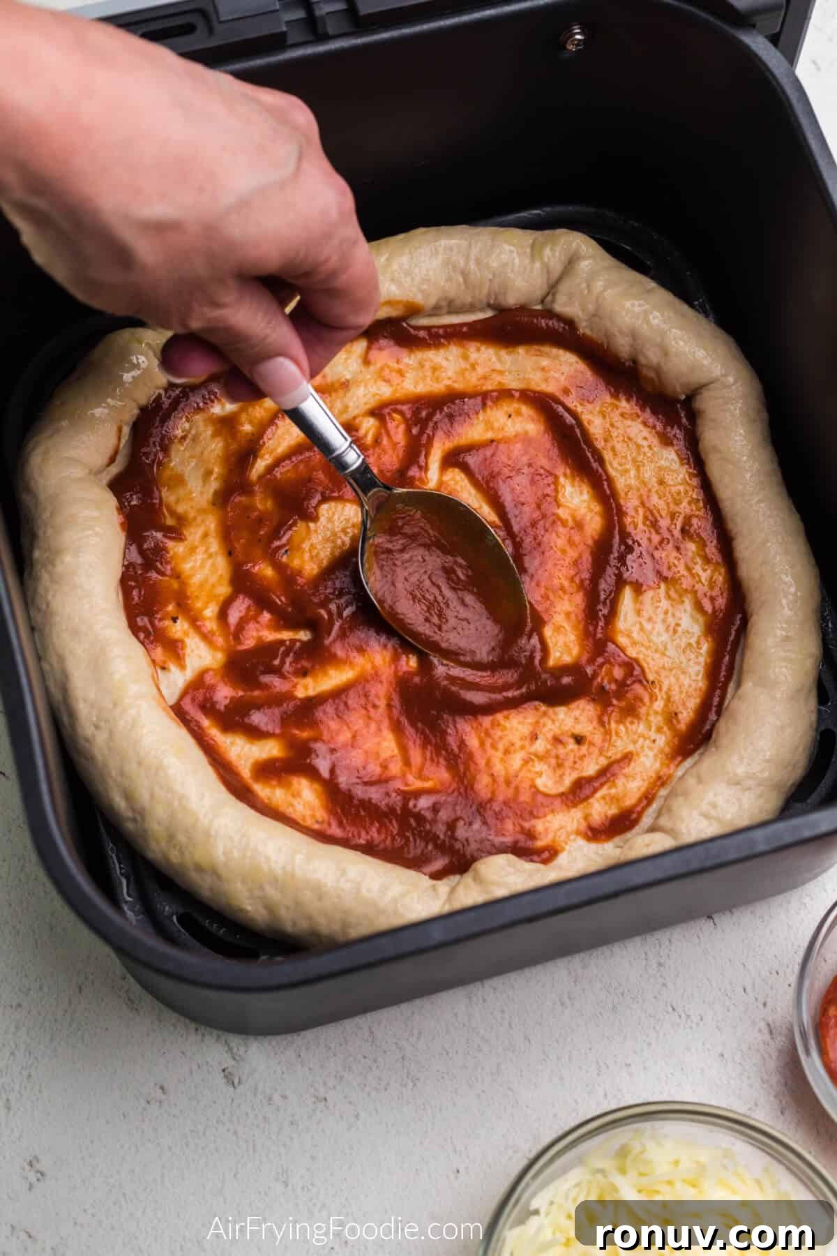 Pizza sauce being spooned and spread onto the pizza crust.