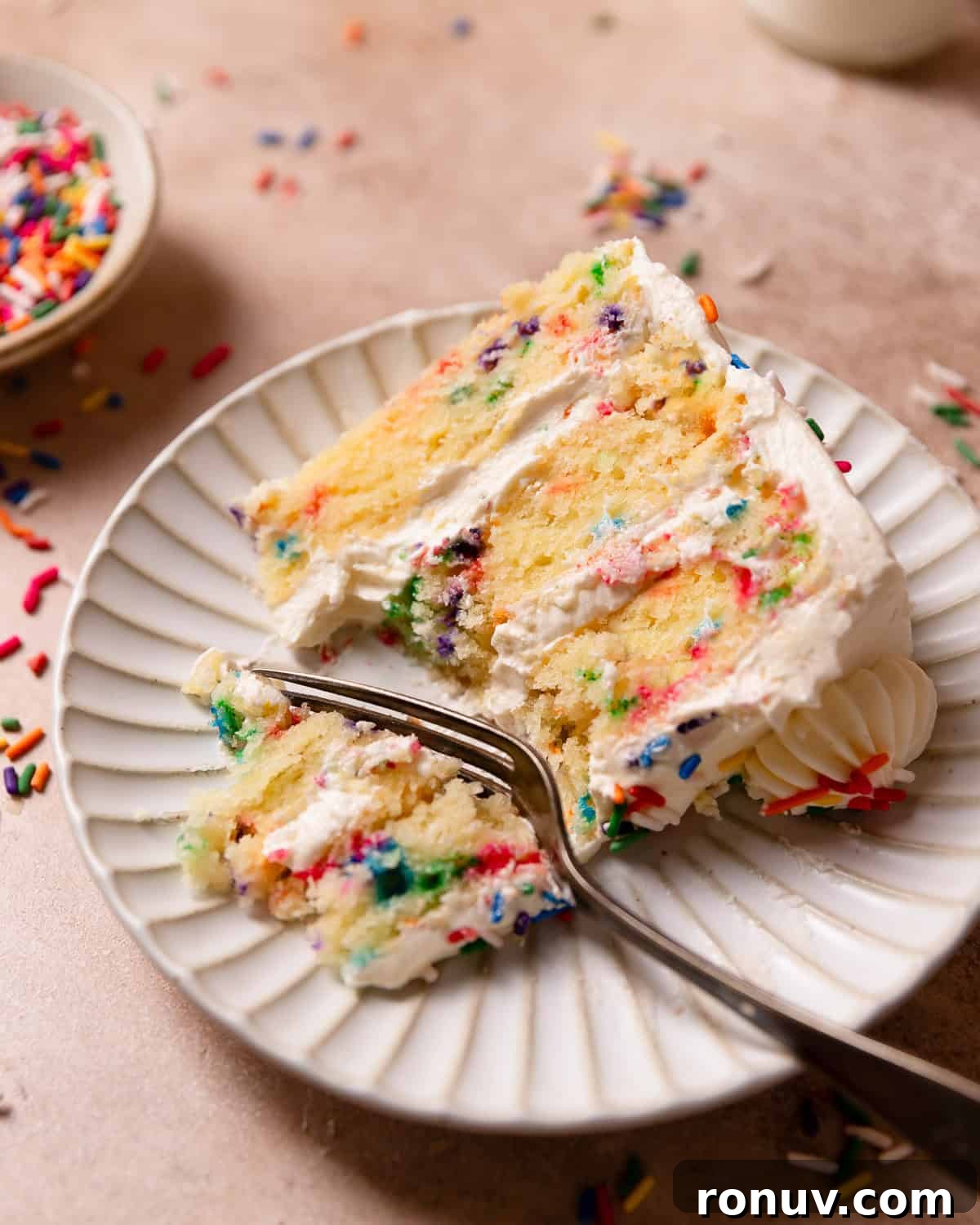 Homemade Funfetti Cake That Beats the Bakery 10 A slice of confetti cake on a white plate with a fork cutting out a bite.