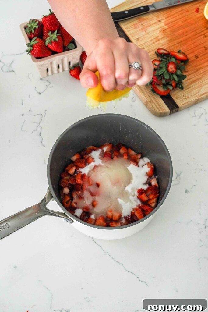How to Make Small-Batch Strawberry Jam 5 A hand squeezes lemon juice into a pot with diced strawberries and sugar.