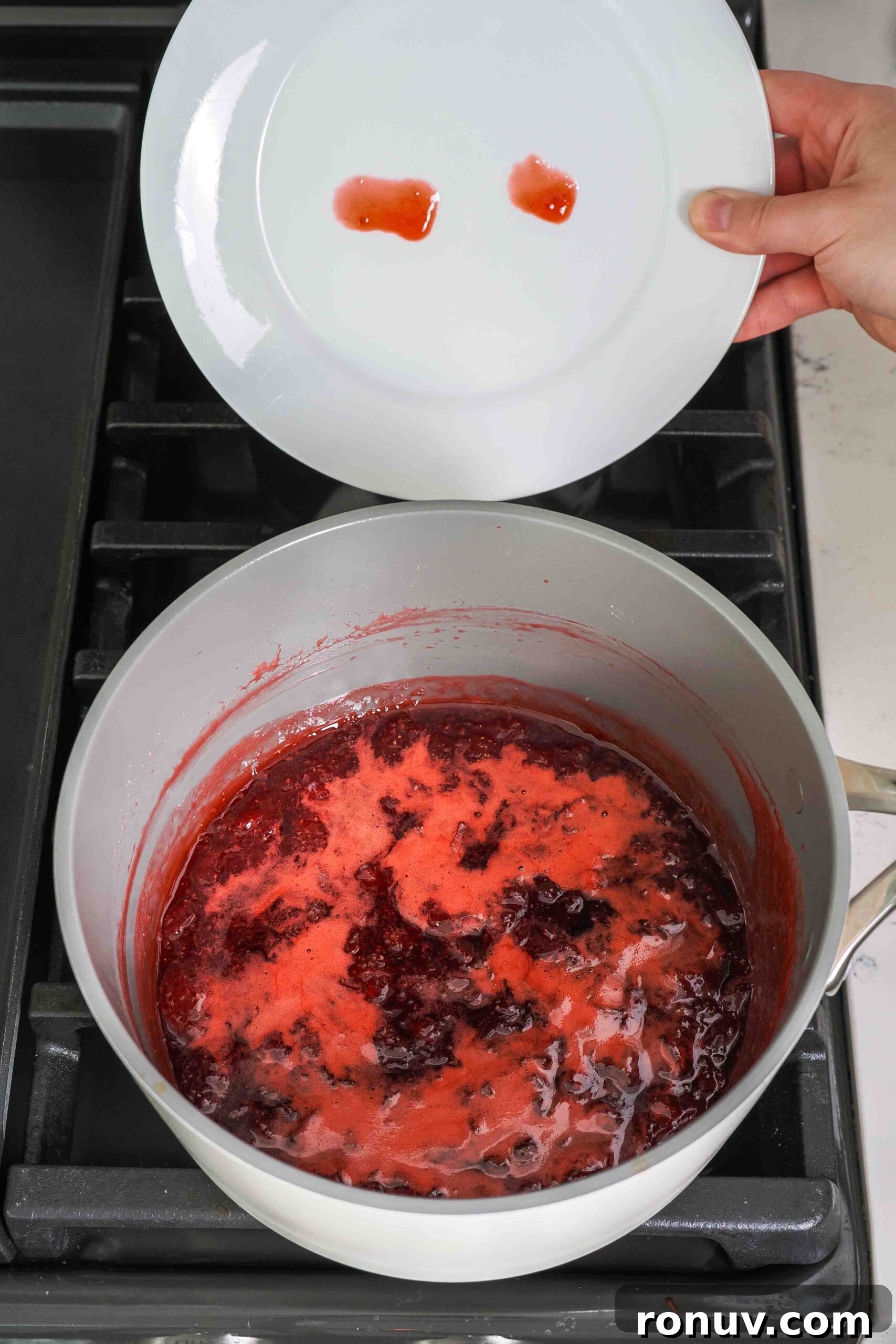 How to Make Small-Batch Strawberry Jam 9 A plate with two dots of strawberry jam on it above a pot of strawberry jam. One dot is runny; the other is more circular.