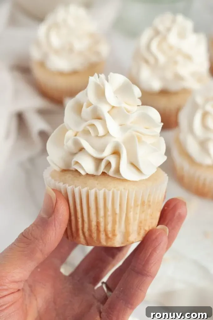 Gluten-Free Cupcakes: Moist, Bakery-Style Recipes 3 A hand is holding a vanilla cupcake that is topped with white fluffy buttercream frosting.