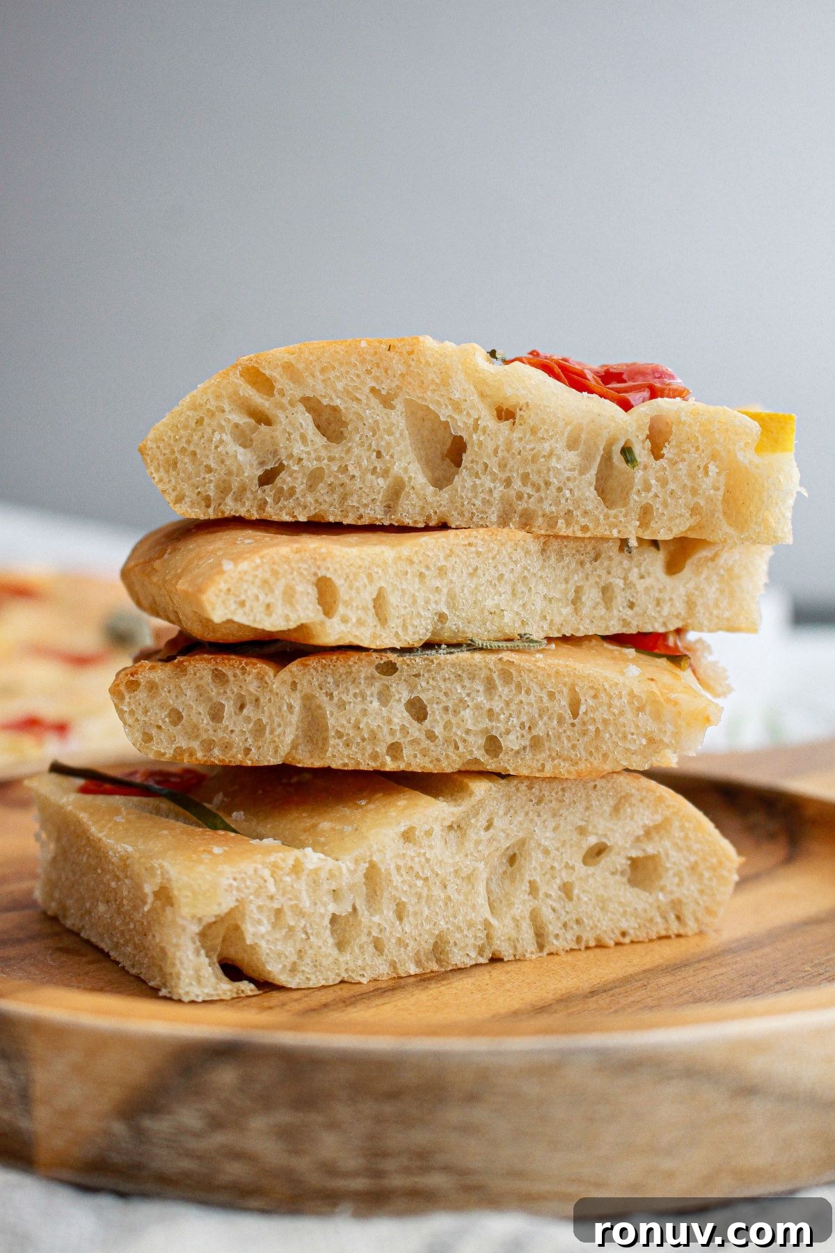 Tomato Focaccia: Classic Italian Bread 10 four pieces of tomato focaccia bread stacked on a wooden cutting board.