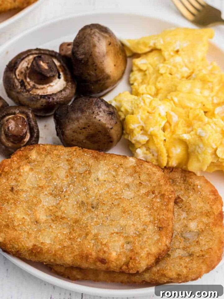 plate with 2 hash brown patties on it, with scrambled eggs and mushrooms in the back