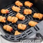 Pigs in blankets cooking in an air fryer basket.