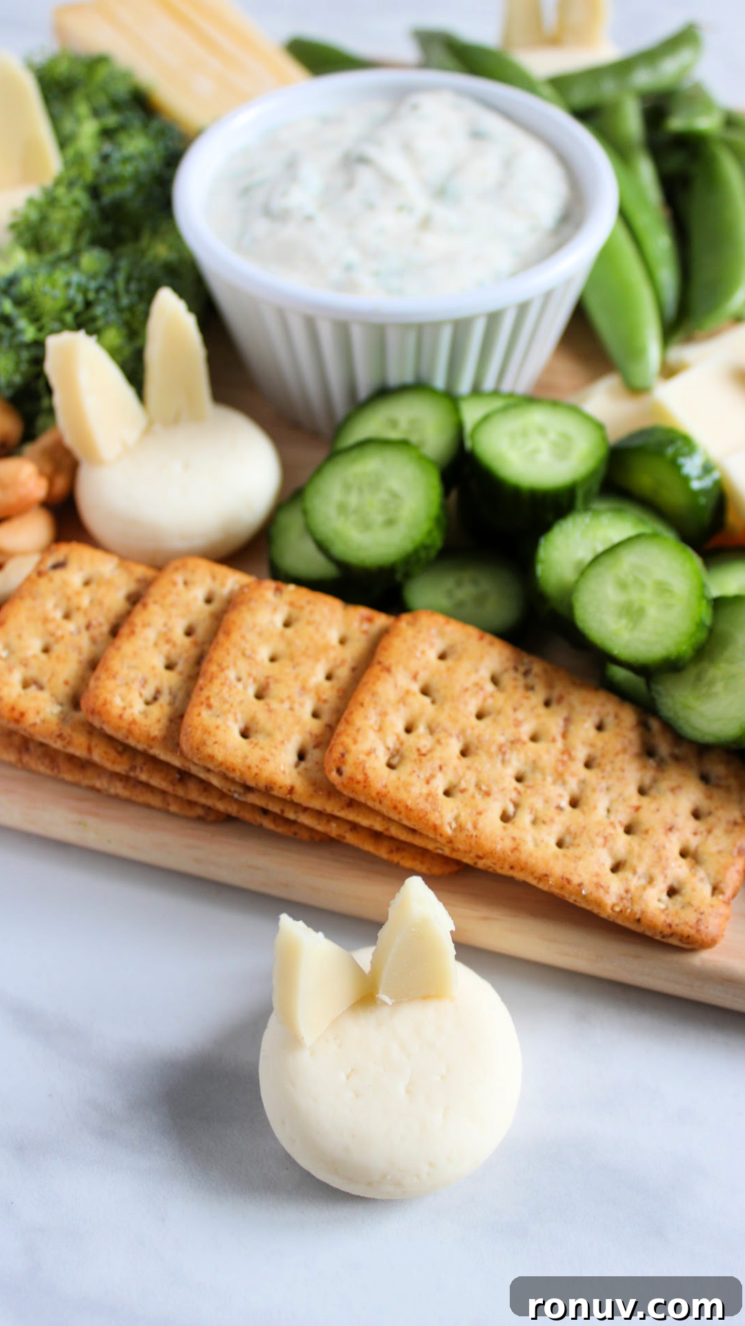 DIY Adorable Easter Charcuterie Board Ideas 3 Overhead view of an Easter charcuterie board with dip, green vegetables, crackers, and bunny cheese
