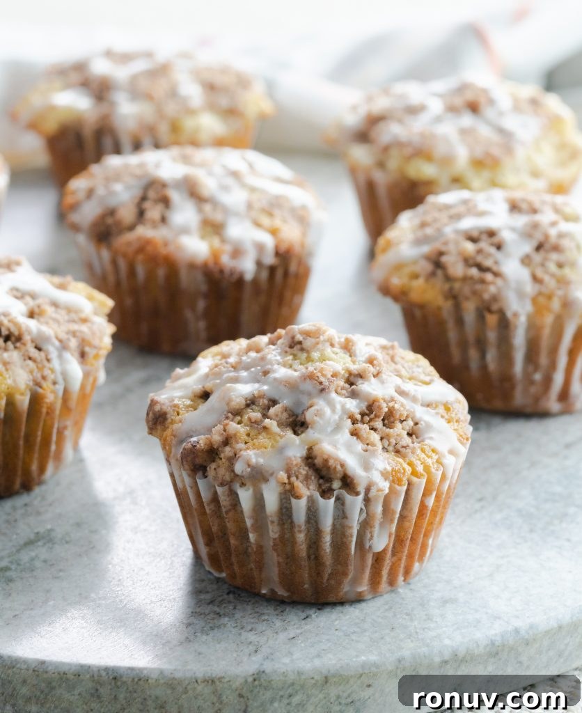 A sour cream coffee cake muffin with a streusel topping and glaze. Close up of sour cream coffee cake muffin with sweet glaze on gray circular board.